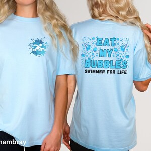 May include: Light blue t-shirt with a swimmer graphic on the front and the text "Eat My Bubbles Swimmer For Life" on the back.