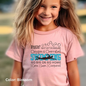 May include: A pink t-shirt with a blue and black graphic that says "Breathe? Eat my bubbles. Oxygen is overrated. Swimming. Go big or go home. I came. I swam. I conquered."