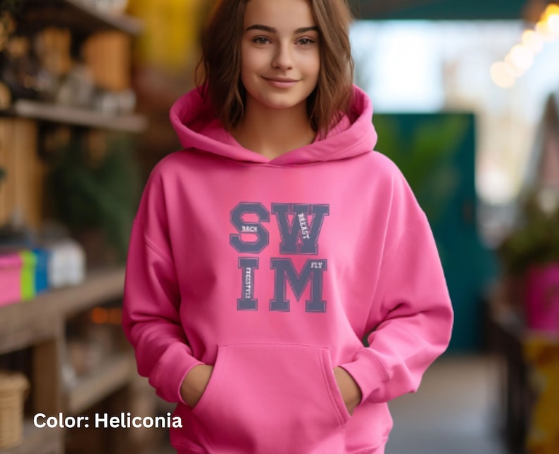 May include: A pink hoodie with a front pocket and a drawstring hood. The hoodie features the word "SWIM" in a collegiate-style font, with the words "BACK", "BREAST", "FLY", and "FREESTYLE" arranged around it. The color is Heliconia.