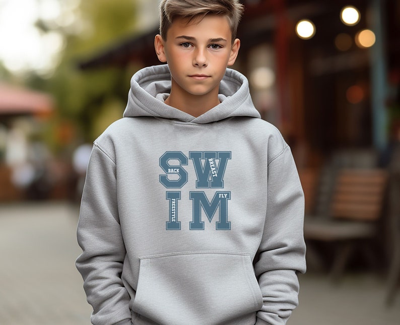 May include: A light gray hoodie with a front pocket and a drawstring hood. The front of the hoodie features the word "SWIM" in a blue, collegiate-style font, with "BACK", "BREAST", "FREESTYLE", and "FLY" arranged around the letters.