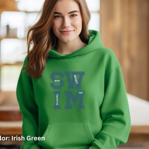 May include: Irish green hoodie with the word SWIM in large, teal letters. The words BACK, BREAST, FREESTYLE, and FLY are stacked around the SWIM letters. The hoodie has a drawstring hood and a front pocket.