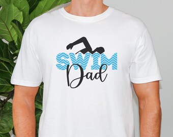 May include: White t-shirt with a black swimmer graphic above the words "Swim Dad" in blue and black. The word "Swim" is in a blue chevron pattern.