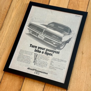 May include: Framed vintage advertisement featuring a classic car, with the text "Turn your pussycat into a tiger." The ad is in black and white, with the car prominently displayed. The frame is black.