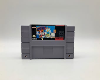 May include: A Super Nintendo Entertainment System (SNES) game cartridge for Mario Paint. The cartridge is gray with a black label featuring a colorful illustration of Mario painting on a canvas.