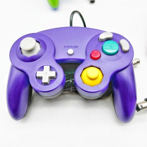May include: A purple GameCube controller with a yellow, red, and green button. The controller has a white plus sign button and a white start/pause button.