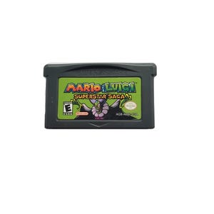 May include: A Game Boy Advance cartridge for the game "Mario & Luigi: Superstar Saga." The label features the game's title in green and yellow, with a cartoon character illustration. The cartridge is dark gray.