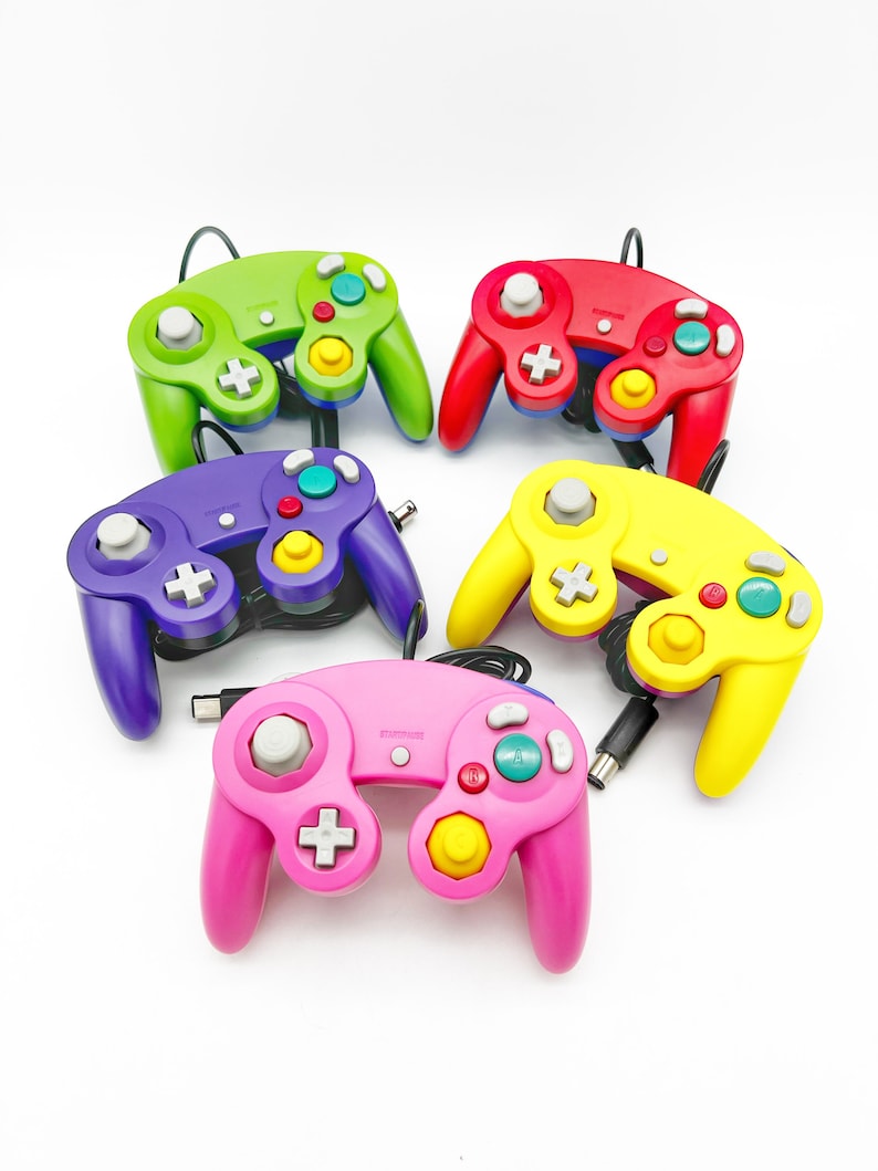 May include: Five colorful GameCube controllers, each with a different color: green, red, purple, yellow, and pink. The controllers are arranged in a circle on a white background.