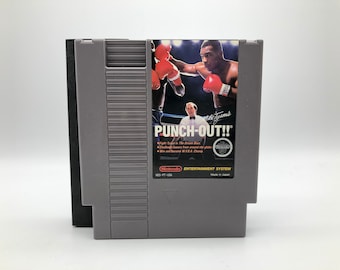 Op de afbeelding: Een grijze Nintendo Entertainment System-spelcartridge voor Punch-Out!! met Mike Tyson op de cover. De spelcartridge heeft een zwart label met de titel van het spel en een wit Nintendo-logo.