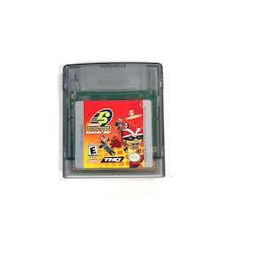May include: A gray Game Boy Color game cartridge with a red, yellow, and blue label. The label features the text "Rocket Power: Gettin' Air" and a cartoon image of a group of characters. The game is rated "E" for Everyone by the ESRB.
