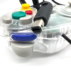May include: A clear, transparent GameCube controller with a black cable and a blue button. The controller has a green, yellow, and red button.