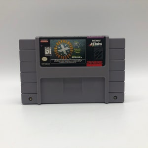 May include: A gray Super Nintendo game cartridge with a black label. The label features the text "Revolution X" in a yellow circle with a black X in the center. The text "Back in the 8-bit groove" is also on the label. The label also includes the text "Midway" and "Acclaim".