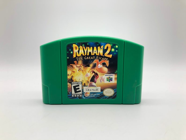May include: Green Nintendo 64 game cartridge for Rayman 2: The Great Escape. The front of the cartridge features a colorful image of Rayman and other characters from the game. The game is rated E for Everyone by the ESRB.