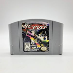 以下が含まれることがあります： Re-VoltというゲームのグレーのNintendo 64ゲームカートリッジ。ゲームカートリッジには、おもちゃの車がトラックでレースをしているカラフルな画像が描かれています。このゲームはESRBによってE for Everyoneと評価されています。