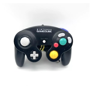 May include: A black Nintendo GameCube controller with white, yellow, green, blue, and red buttons. The controller has a white circular button on the top.