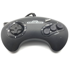 Może przedstawiać: Czarny kontroler Sega Genesis z układem sześciu przycisków. Kontroler posiada krzyżak, przyciski start i tryb, a także trzy przyciski czołowe oznaczone literami A, B i C. Słowo "TRIGGER" jest nadrukowane na kontrolerze.