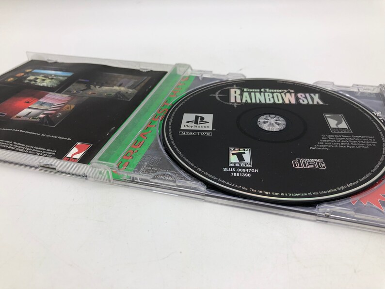 Puede incluir: Una caja de juego de PlayStation para Tom Clancy's Rainbow Six. La caja es negra con un borde verde y blanco. El disco del juego es visible dentro de la caja. El juego est&aacute; clasificado como T para adolescentes por la ESRB.