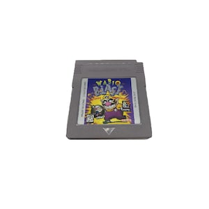 Könnte beinhalten: Eine graue Game Boy Color-Cartridge mit einem lila, gelben und blauen Etikett. Das Etikett lautet "Wario Blast! Featuring Wario & Waluigi".