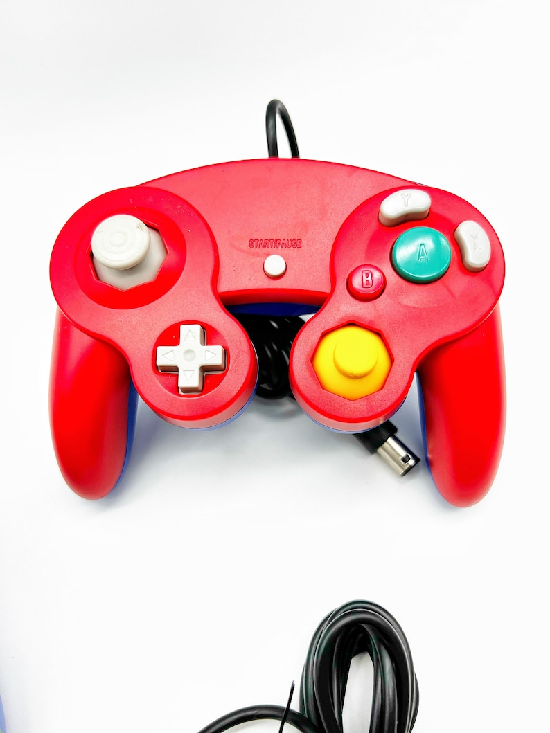 May include: A red and blue GameCube controller with a yellow button and a white start/pause button. The controller is connected to a black cord.