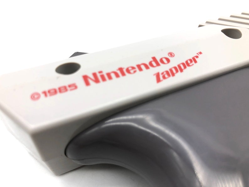 May include: A white and gray Nintendo Zapper light gun with the text "&copy;1985 Nintendo&reg; Zapper&trade;" printed on the top.