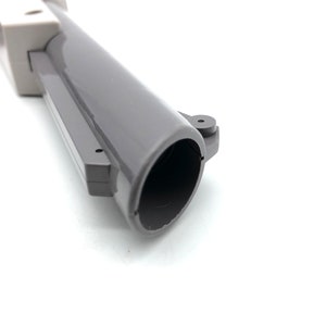 May include: Close-up of the barrel of a gray plastic toy gun. The barrel is hollow and has a black interior.