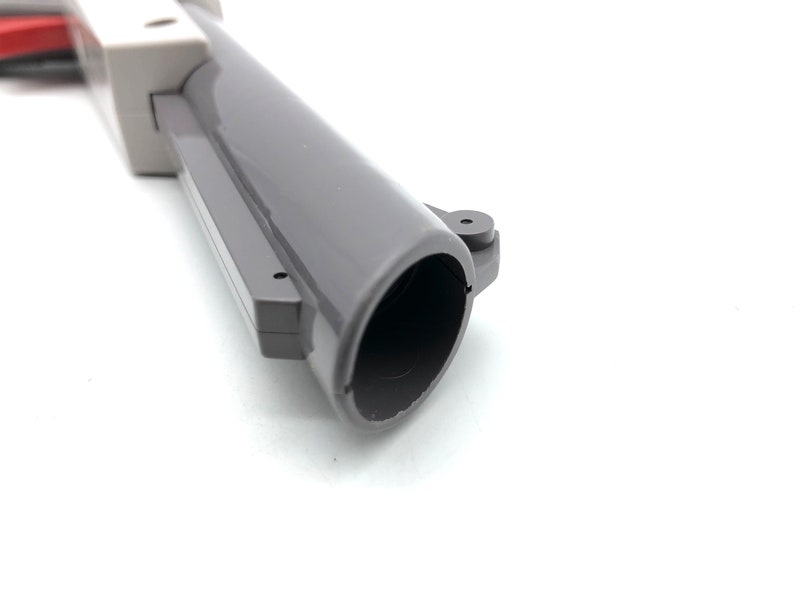 May include: Close-up of the barrel of a gray plastic toy gun. The barrel is hollow and has a black interior.