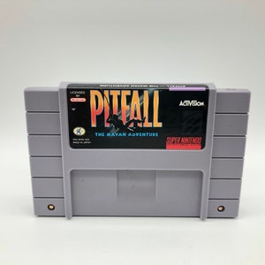 May include: A gray Super Nintendo Entertainment System game cartridge with a black label. The label features the text "Pitfall: The Mayan Adventure" in orange and yellow lettering. The Activision logo is in the upper right corner, and the Super Nintendo logo is in the lower right corner.