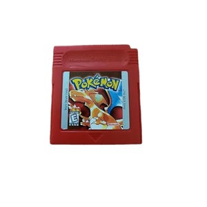 Puede incluir: Cartucho rojo de Nintendo Game Boy para el juego "Pokemon". La etiqueta presenta el logotipo de Pokemon y una ilustración de Charizard. El cartucho está marcado "THIS SIDE OUT" y "DMG-A-USA."