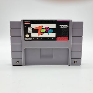 Puede incluir: Un cartucho de juego Super Nintendo Entertainment System gris con una etiqueta negra. La etiqueta presenta un logotipo colorido para el juego "Top Loop" y el texto "Viacom" y "Super Nintendo Entertainment System".
