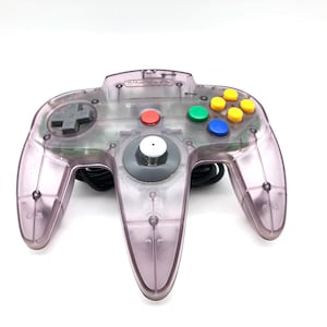 Puede incluir: Un mando de Nintendo 64 de color púrpura transparente con un cable negro. Cuenta con una cruceta gris, botones rojos, verdes, azules y amarillos, y un joystick gris. El logotipo de Nintendo es visible.