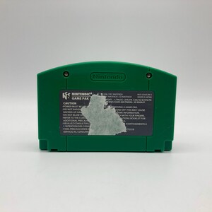 May include: Green Nintendo 64 game cartridge with a black label that reads "Nintendo 64 Game Pak" and includes a warning label. The label also includes the text "Caution: Power must be turned off before removing a game pak and off this may cause game information to be lost. Do not touch the connector with your fingers. Refer to the control instructions booklet for additional precautions."