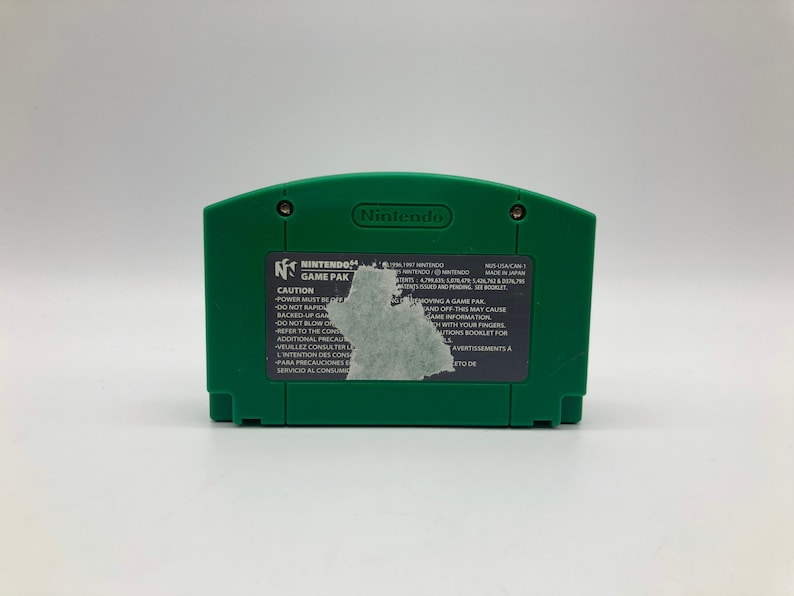 May include: Green Nintendo 64 game cartridge with a black label that reads "Nintendo 64 Game Pak" and includes a warning label. The label also includes the text "Caution: Power must be turned off before removing a game pak and off this may cause game information to be lost. Do not touch the connector with your fingers. Refer to the control instructions booklet for additional precautions."