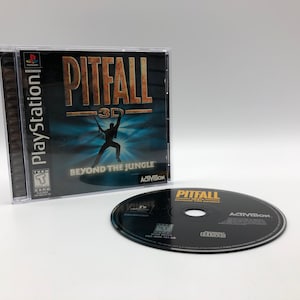 Può includere: Una custodia per gioco PlayStation per Pitfall 3D: Beyond the Jungle, con un design nero e oro con una silhouette di una persona che tiene una corda. Il gioco è classificato T per Teenager dalla ESRB.