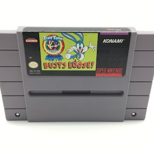 May include: A gray Super Nintendo Entertainment System game cartridge with a blue, red, and yellow label. The label features a cartoon rabbit and the text "Tiny Toon Adventures: Buster Busts Loose!" and "Konami".