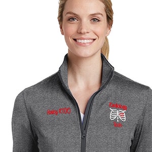 May include: A heather gray zip-up jacket with a red embroidered logo on the right side. The logo features a ribcage with the text "Radiology" and "Tech" underneath.