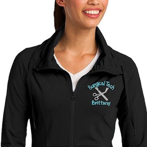 May include: Black zip-up jacket with a mock neck collar. The jacket has a small embroidered design on the left chest that says "Surgical Tech" with a pair of scissors and the name "Brittany" underneath.