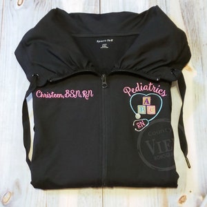 May include: Black zippered jacket with pink embroidery that says "Pediatrics" with a heart and blocks that say "ABC" and a stethoscope with "RN" on it. The left side of the jacket has pink embroidery that says "Christen, BSN, RN".