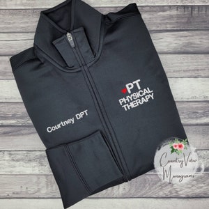 May include: Black zip-up jacket with a white embroidered logo that says "PT Physical Therapy" and a red heart. The name "Courtney DPT" is embroidered on the left sleeve.