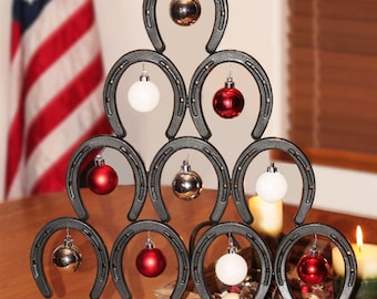 May include: A black metal Christmas tree made of horseshoes with red and white ornaments. The tree is decorated with a red star on top and is sitting on a wooden table.