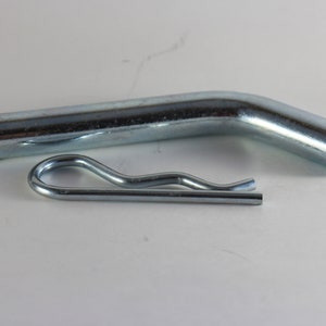 May include: A silver metal hitch pin with a bent end and a silver metal clip.