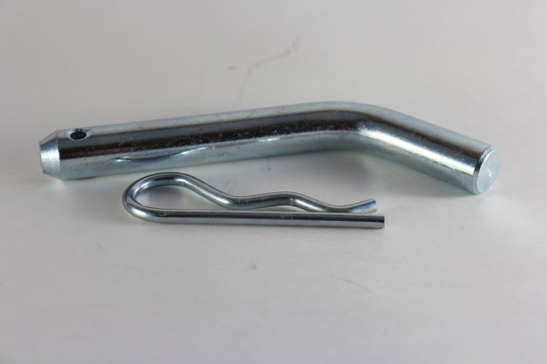May include: A silver metal hitch pin with a bent end and a silver metal clip.