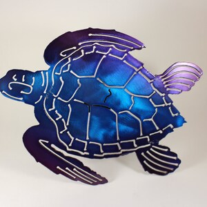 May include: A metal sea turtle sculpture with a blue and purple ombre finish. The turtle is in a swimming pose with its flippers outstretched.