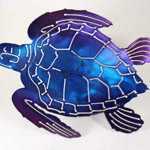 May include: A metal sea turtle wall art sculpture with a blue and purple iridescent finish. The turtle is in a swimming pose with its head turned to the side. The shell is detailed with a pattern of lines and shapes.
