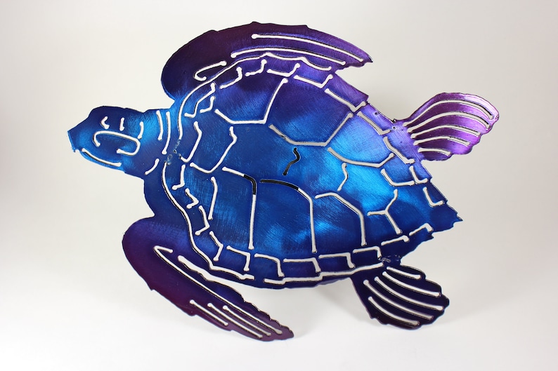May include: A metal sea turtle wall art sculpture with a blue and purple iridescent finish. The turtle is in a swimming pose with its head turned to the side. The shell is detailed with a pattern of lines and shapes.