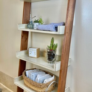 Puede incluir: Estanter&iacute;a de escalera de madera r&uacute;stica con cuatro estantes blancos y soportes de madera marr&oacute;n. Los estantes exhiben una variedad de accesorios de ba&ntilde;o, incluyendo toallas, plantas, una vela y una cesta tejida. El calendario indica mi&eacute;rcoles 23 de noviembre.