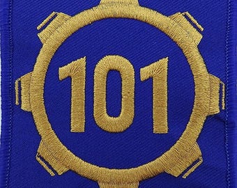 May include: A blue embroidered patch featuring a gold gear design with the number 101 in the center. The patch has a square shape with a stitched border, suitable for sewing or ironing onto fabric.