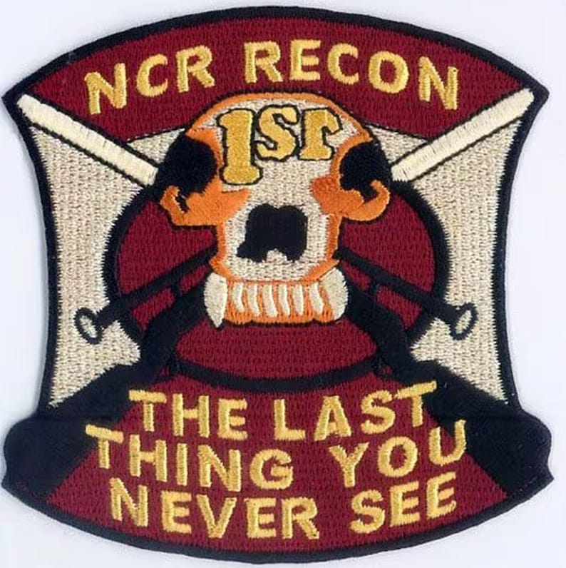 May include: A maroon and white embroidered patch with a skull and crossbones design. The skull has the number "1ST" on its forehead. The text "NCR RECON" is at the top of the patch. The text "THE LAST THING YOU NEVER SEE" is at the bottom of the patch.