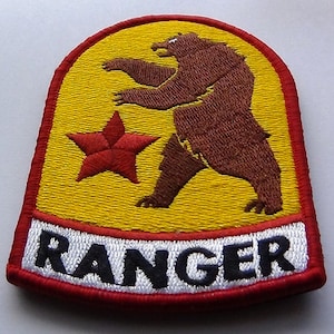 May include: A yellow and red embroidered patch with a brown bear standing on its hind legs. A red star is to the left of the bear. The text "RANGER" is in black letters on a white background at the bottom of the patch.