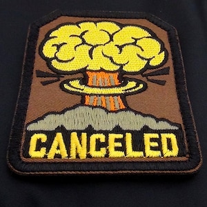 May include: A brown and black embroidered patch featuring a yellow cartoon mushroom cloud and the word "CANCELED" in yellow lettering.
