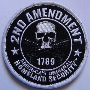 Könnte beinhalten: Ein gestickter schwarzer und weißer Aufnäher mit Totenkopf und gekreuzten Knochen, dem Text "2nd Amendment", "America's Original Homeland Security" und dem Jahr "1789".