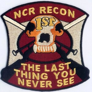 May include: A maroon and beige embroidered patch with a skull and crossbones design. The skull is orange and has the letters "ISF" on its forehead. The patch has the text "NCR RECON" at the top and "THE LAST THING YOU NEVER SEE" at the bottom.